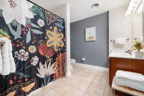 Casa de banho com cortina de chuveiro estampada com motivos florais, sanita, lavatório com espelho e porta-toalhas.