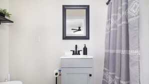 Un baño con un lavamanos blanco, un espejo, un ventilador de techo y una cortina de ducha.