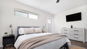 Un dormitorio moderno con cama, mesitas de noche, cómoda, televisor y ventana.