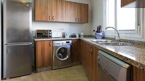 Une cuisine moderne dotée d’appareils électroménagers en acier inoxydable, de meubles de rangement en bois, d’un lave-linge encastré et d’un plan de travail en granit.