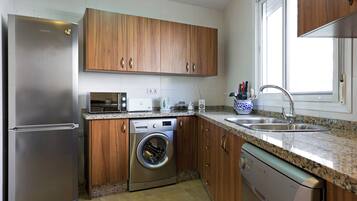 Een moderne keuken met roestvrijstalen apparatuur, houten keukenkastjes, een ingebouwde wasmachine en een granieten aanrecht.
