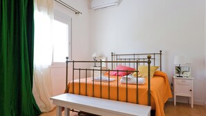 Une chambre à coucher comprenant un lit, une table de chevet, une fenêtre avec des rideaux et un appareil de climatisation.