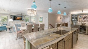 A modern kitchen with a marble island, pendant lights, and a dining area with wicker furniture. - Octopus Cottage: 1.5 Blocks to Beach, Pool & Spa by Anna Maria Life Vacation Rentals (Holmes Beach)