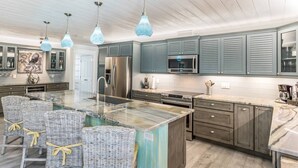 A modern kitchen with a central island, grey cabinetry, and hanging pendant lights. - Octopus Cottage: 1.5 Blocks to Beach, Pool & Spa by Anna Maria Life Vacation Rentals (Holmes Beach)