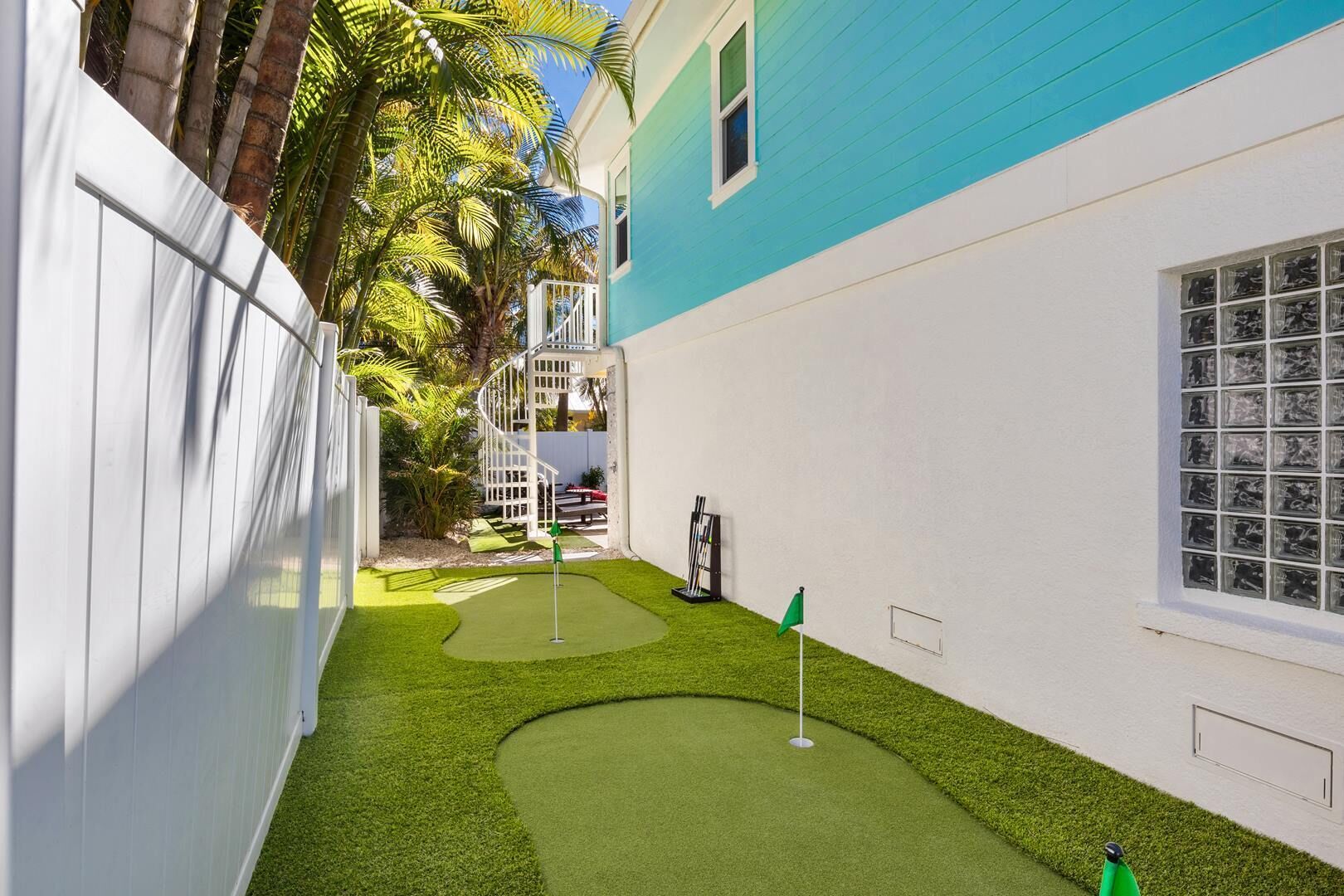Ein kleiner Garten mit Kunstgrasanlage, einem Putting-Green und einem weißen Zaun.