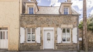 A stone building with a white door, shutters, and a small window.