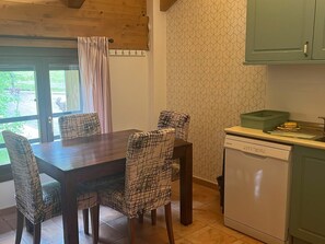 A dining area with a wooden table and patterned chairs, a window with curtains, and a kitchen with a dishwasher and cabinets.