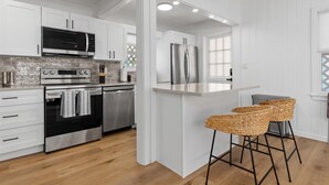 A modern kitchen with white cabinetry, stainless steel appliances, a central island, and two wicker bar stools.