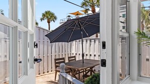 A patio with a wooden table and chairs, a black umbrella, and a white fence.