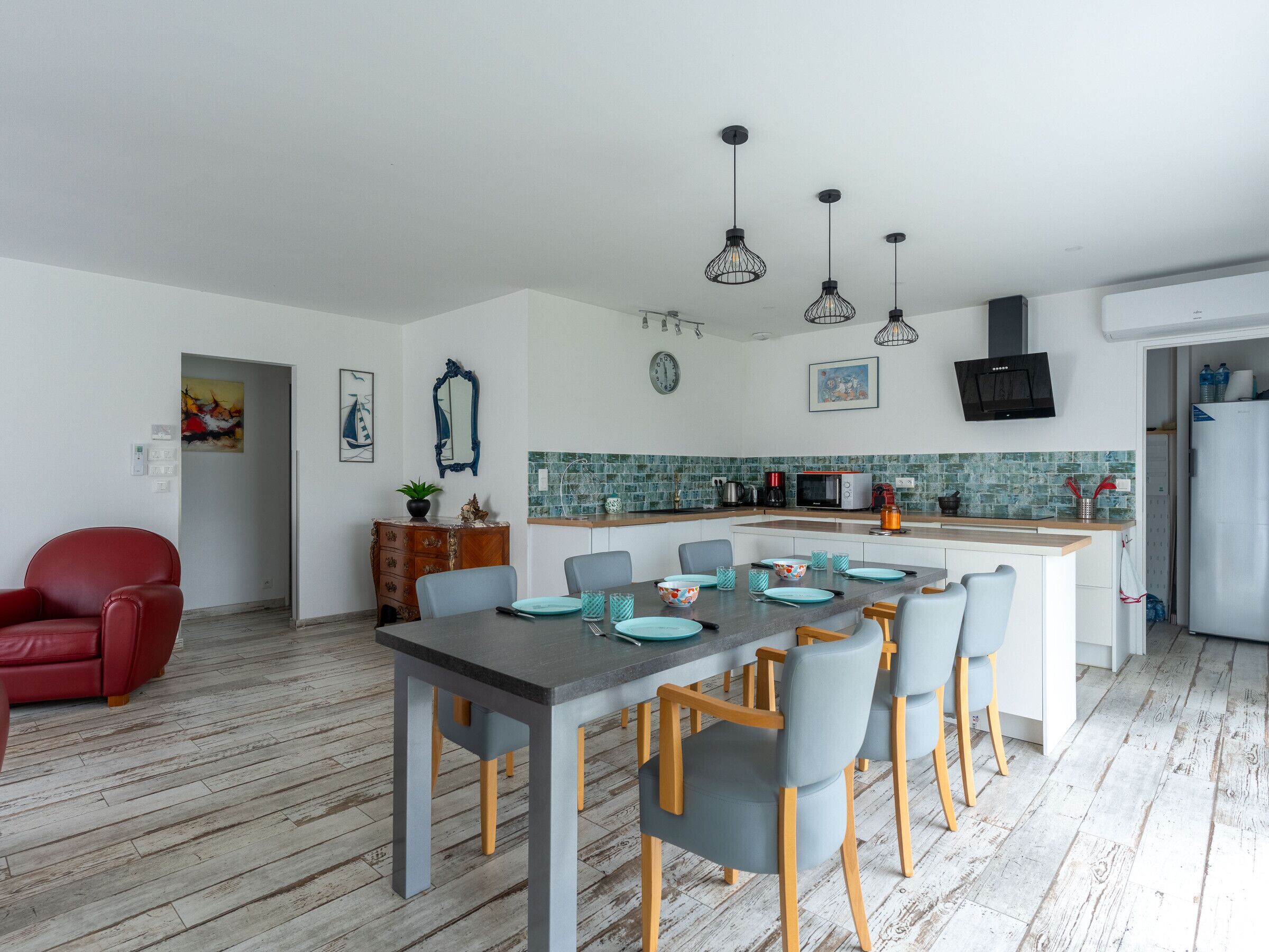 A modern kitchen with a central island, wooden flooring, and pendant lighting.