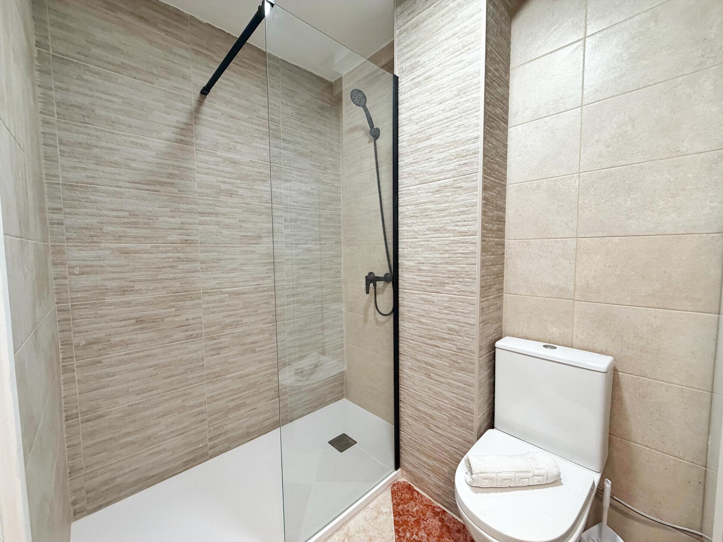 A modern bathroom with a glass-enclosed shower, a white toilet, and a marble floor.