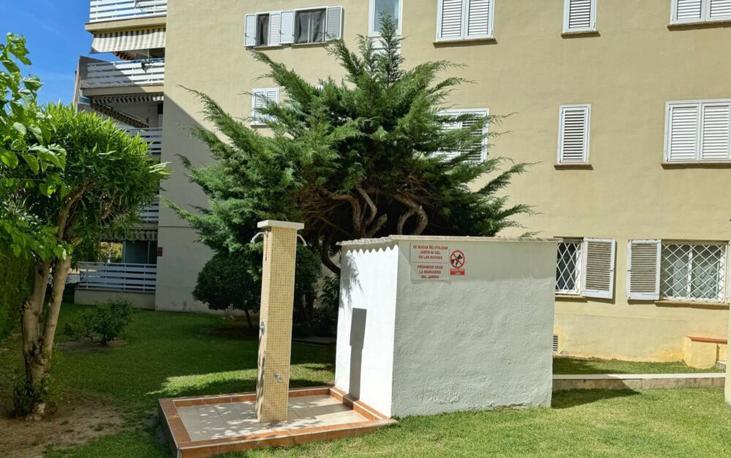 Un bâtiment doté de nombreuses fenêtres et d’un petit espace clos, agrémenté d’un arbre et d’un élément décoratif aquatique.