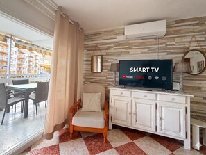 Habitación de hotel con una televisión que muestra 'SMART TV' y servicios de streaming, una silla de madera, un armario blanco y vistas a un balcón con mobiliario exterior.