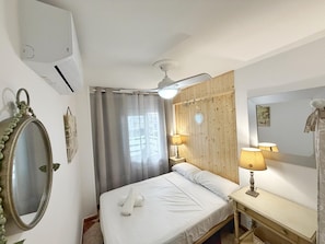 Una habitación con cama, lámparas de noche, un espejo y un ventanal con cortinas.