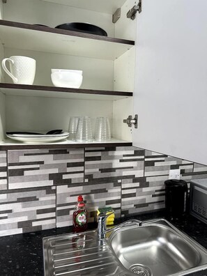 A kitchen with a stainless steel sink, a microwave, and a tiled backsplash.