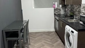 A compact kitchen with a washing machine, a dining area with a table and chairs, and a window with blinds. - 1-bed Apart-nottingham-free Parking (Nottingham)