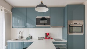 Een moderne keuken met smaragdgroene kastjes, een wit aanrecht, een zwarte hanglamp, een rode koffiezetapparaat en een ingebouwde oven.