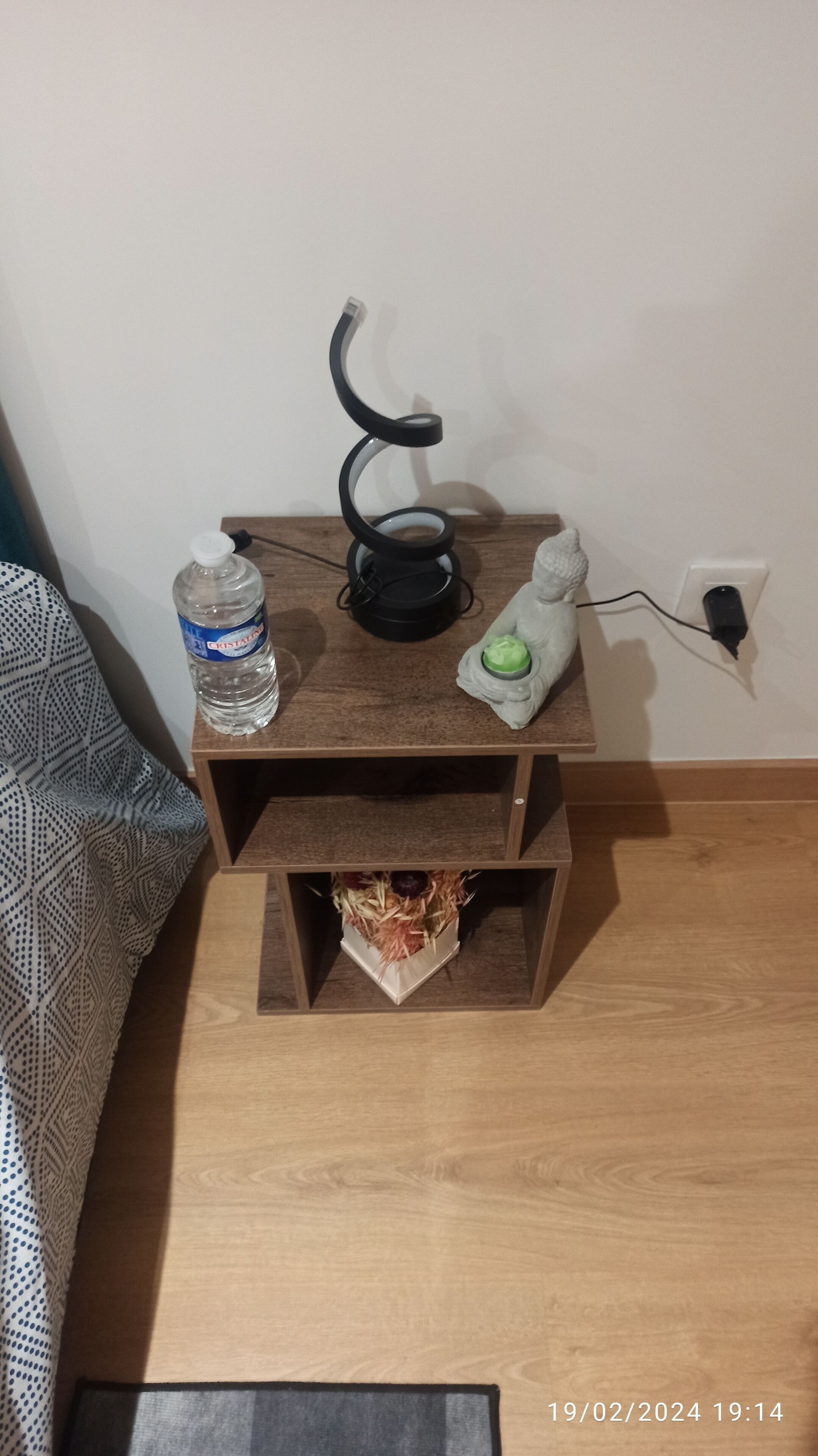 Een klein nachtkastje met een waterfles, een zwarte oplaadkabel en een groen voorwerp.