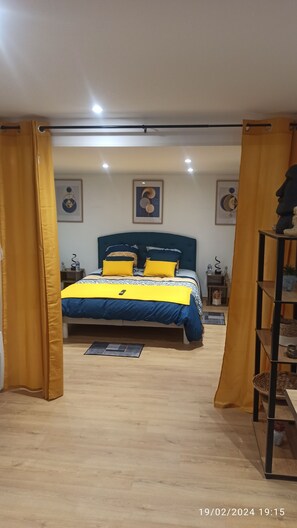 A bedroom with a bed, yellow curtains, a headboard, and artwork on the walls.