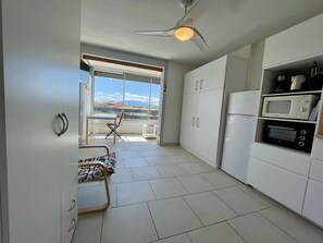 Une cuisine moderne avec des meubles blancs, un réfrigérateur, un four à micro-ondes et un ventilateur de plafond.