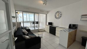 A modern living room with a sofa, a coffee station, and a view of the sea through large windows.