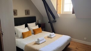 Ein Schlafzimmer mit Bett, Kissen, einem Nachttisch, einem Fenster und einer schrägen Decke.