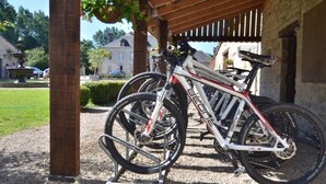 Ein überdachter Fahrradparkplatz mit Kiesboden, einer Holzpergola und einem dahinterliegenden Steinhaus.