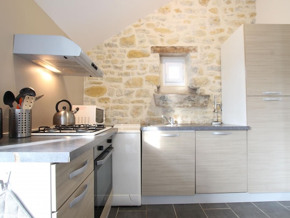 A modern kitchen with a stone wall, a gas stove, a microwave, and wooden cabinets.