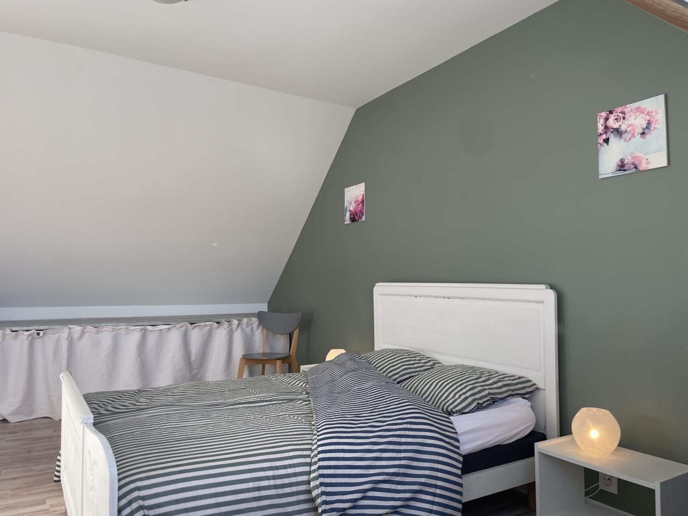 A bedroom with a sloped ceiling, a bed with striped bedding, a bedside table with a lamp, and a chair.