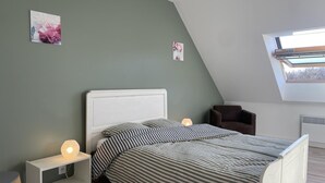 Une chambre avec un plafond en pente, un lit avec une literie à rayures, une table de chevet avec une lampe et une chaise.