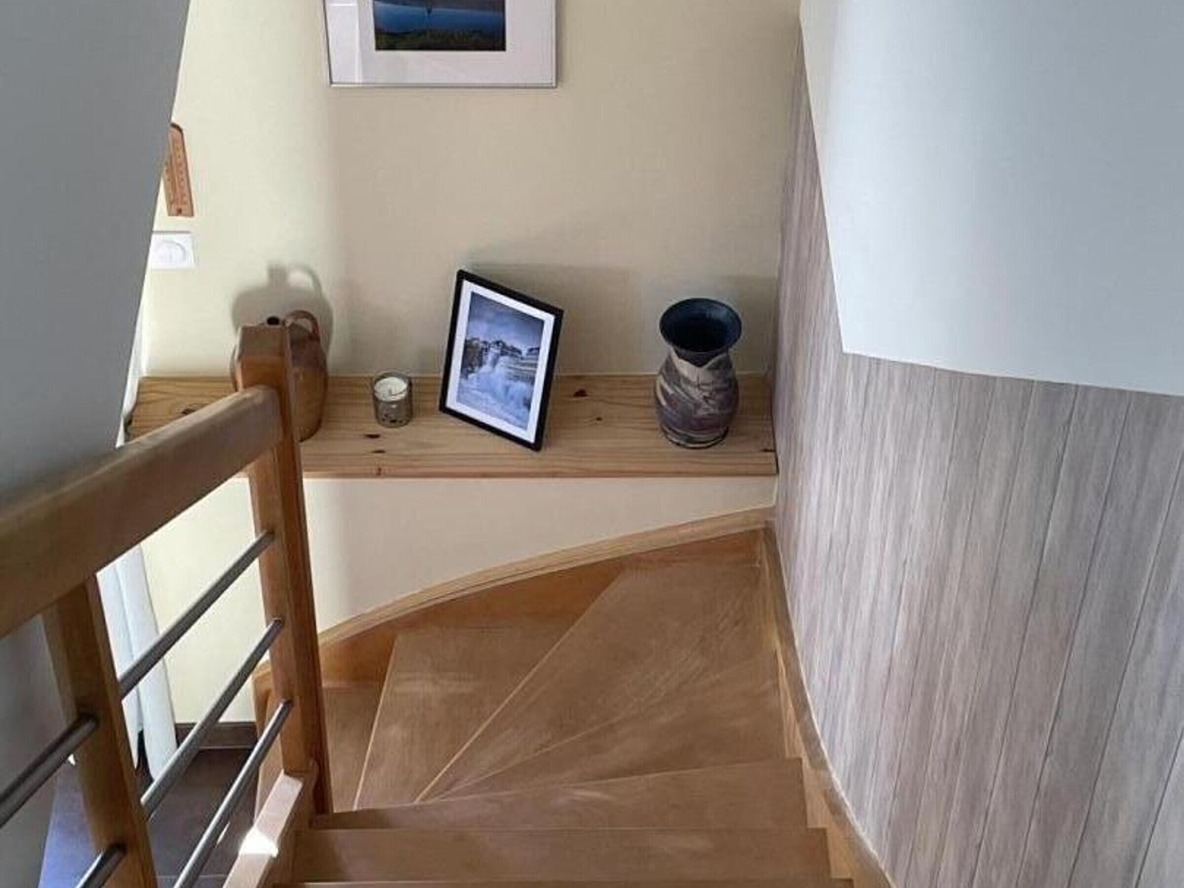 Een houten trap met een leuning, een lijst met een afbeelding, een kaars en een vaas op een plank.