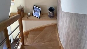 Un escalier en bois avec une rampe, un tableau encadré, une bougie et un vase posés sur une étagère.