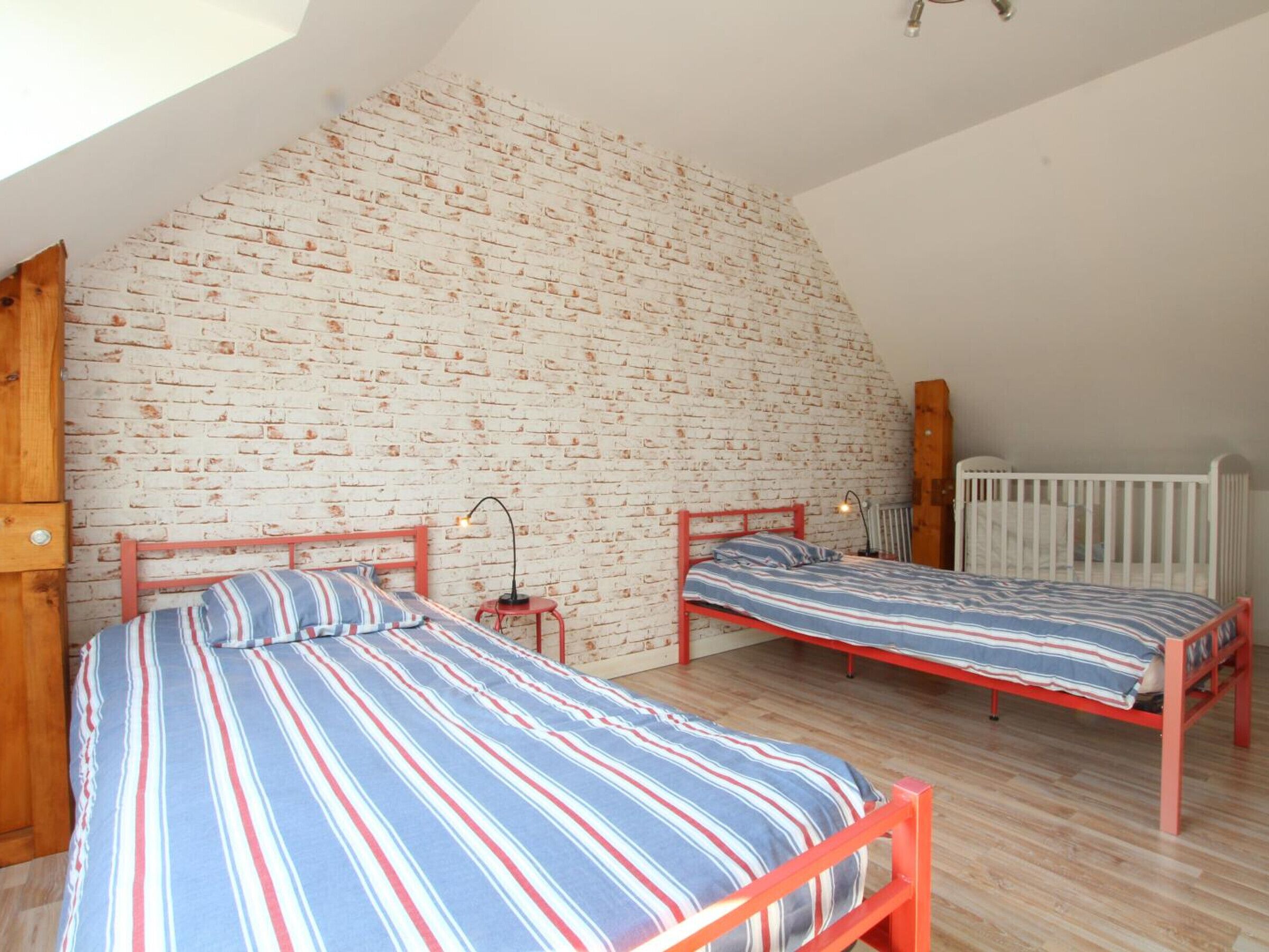 A bedroom with two beds against a white brick wall, wooden floors, and a sloped ceiling.