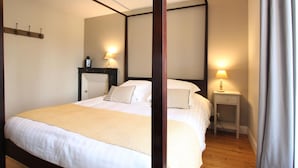 A bedroom with a four-poster bed, two bedside tables with lamps, a wooden floor, and a plain wall. - Charming house with fireplace and pets allowed near Utah Beach (Sainte-Marie-du-Mont)