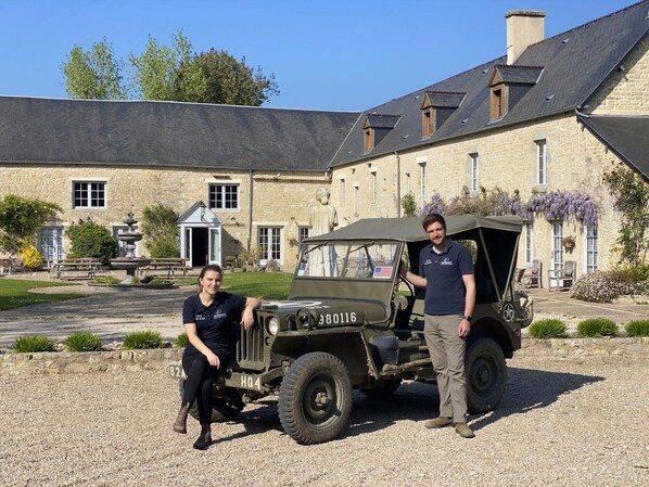 A stone building with a garden and a vintage military jeep.