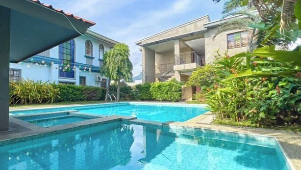 Una piscina con agua cristalina azul, rodeada de exuberante vegetación y edificios modernos.