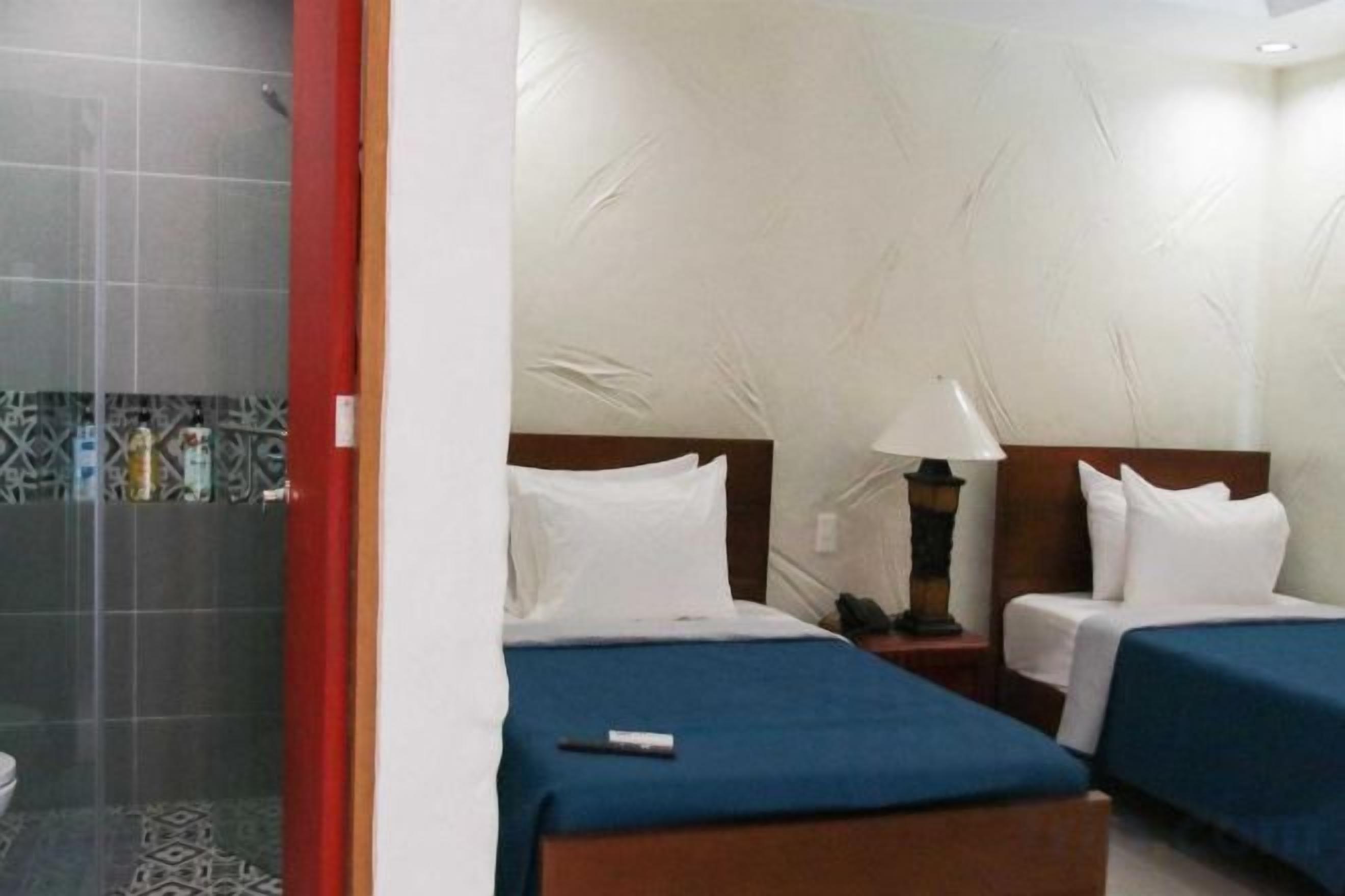 A hotel room with two beds, a nightstand, and a lamp.