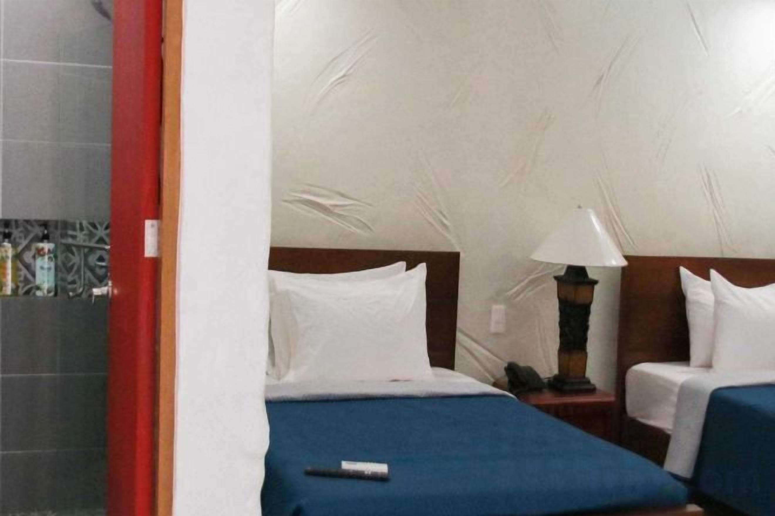 A hotel room with two beds, a nightstand, and a lamp.