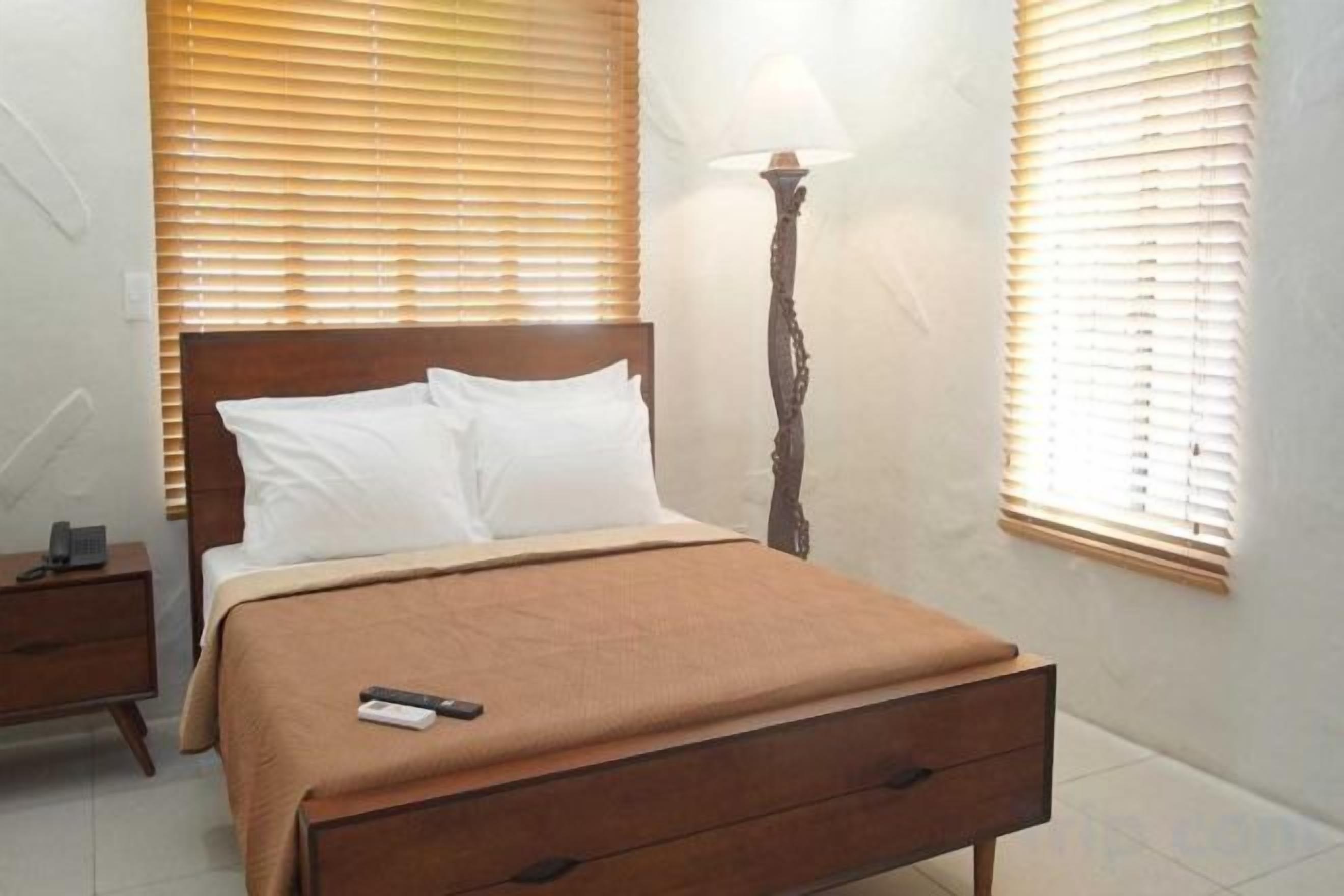 A bedroom with a bed, bedside table, lamp, and window blinds.