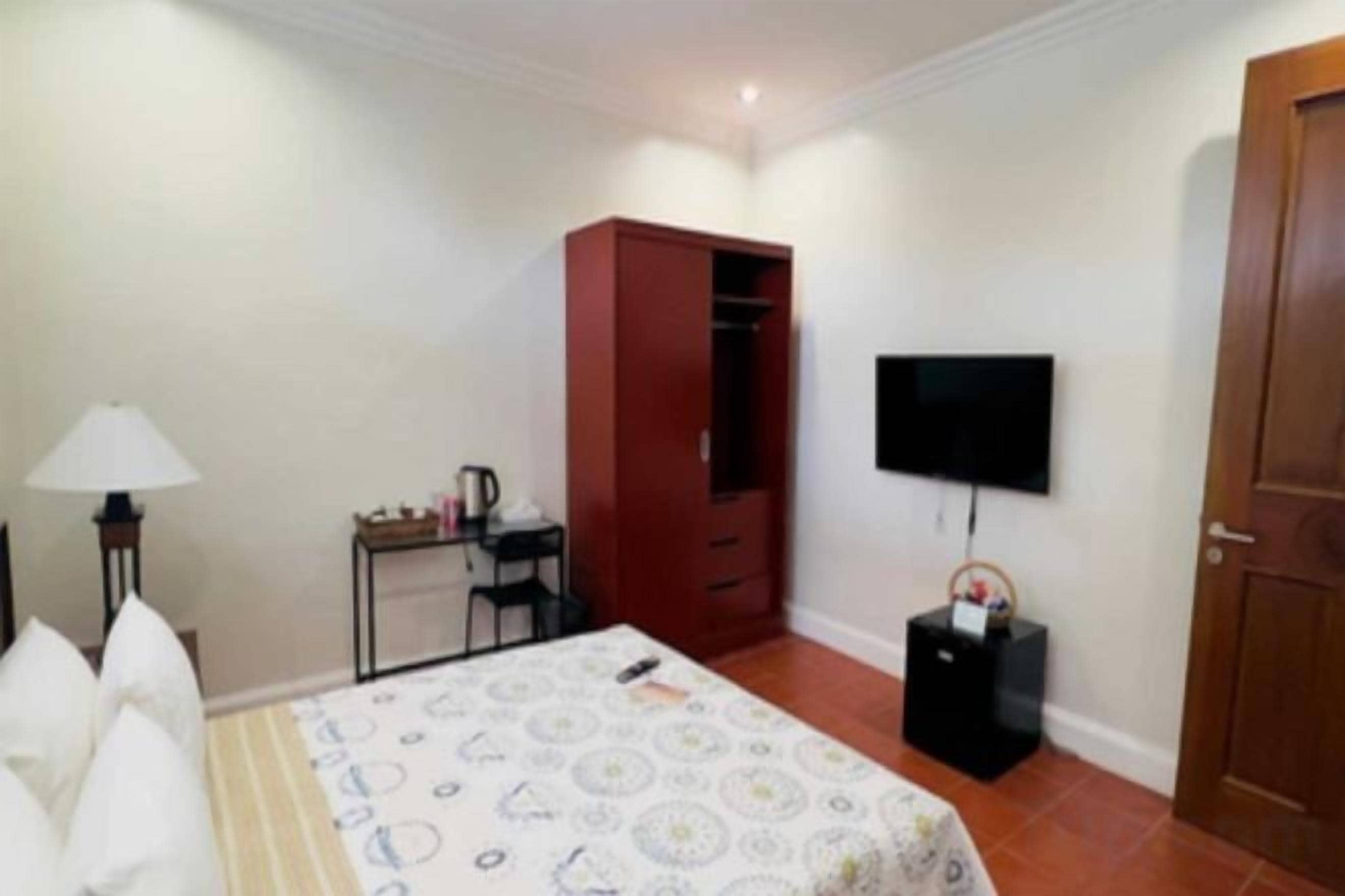 A bedroom with a bed, a wardrobe, a desk, a chair, a television, and a door.