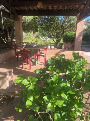 A covered outdoor seating area with a table and chairs, surrounded by greenery and a garden. - Maison de Caractère Plein Centre de st Tropez (Saint-Tropez)