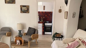 Ein Wohnzimmer mit einer Couch, Sesseln, einem Esstisch und einer Küche im Hintergrund.