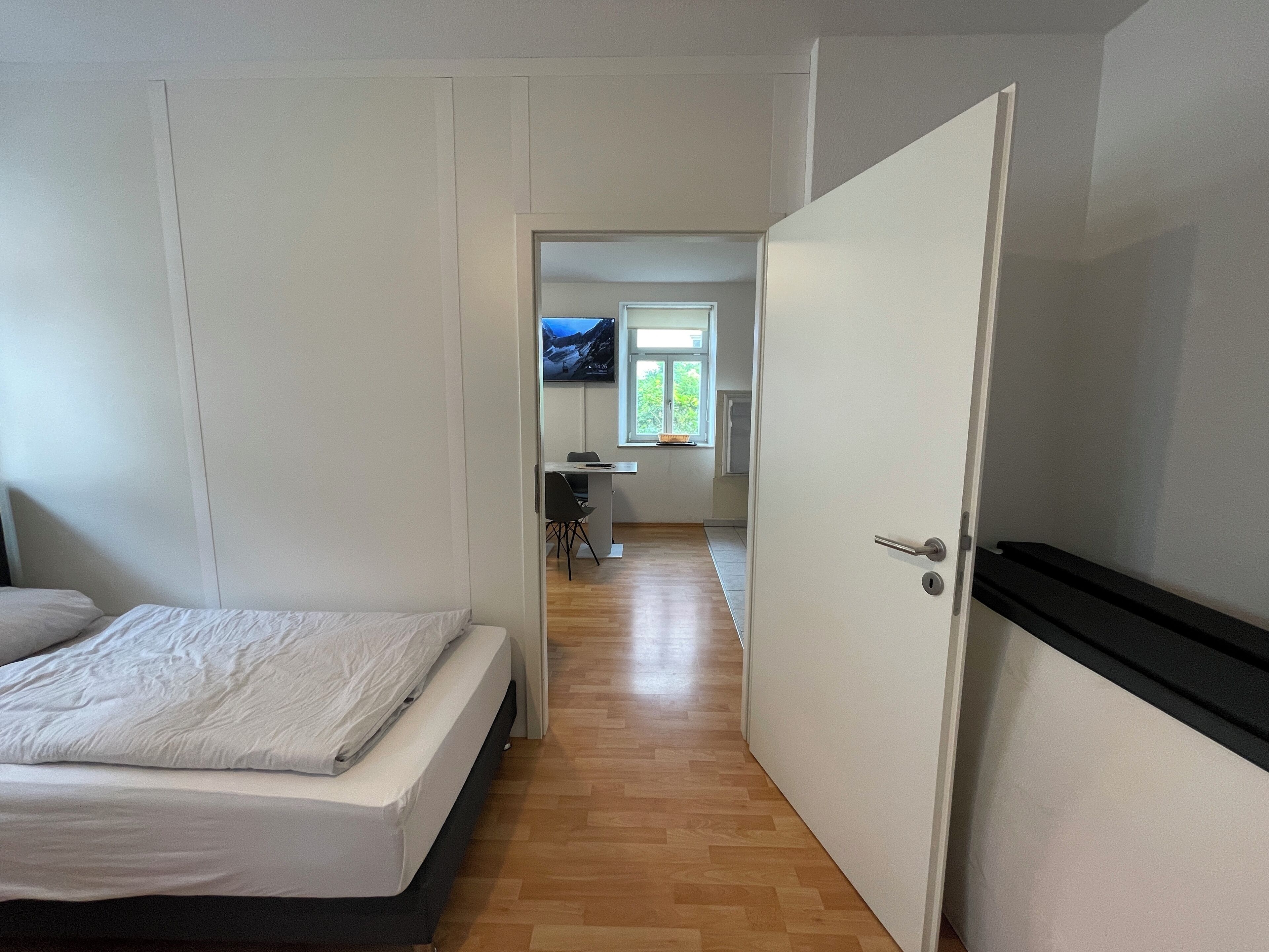 A bedroom with a bed, a desk, and a television in the background.