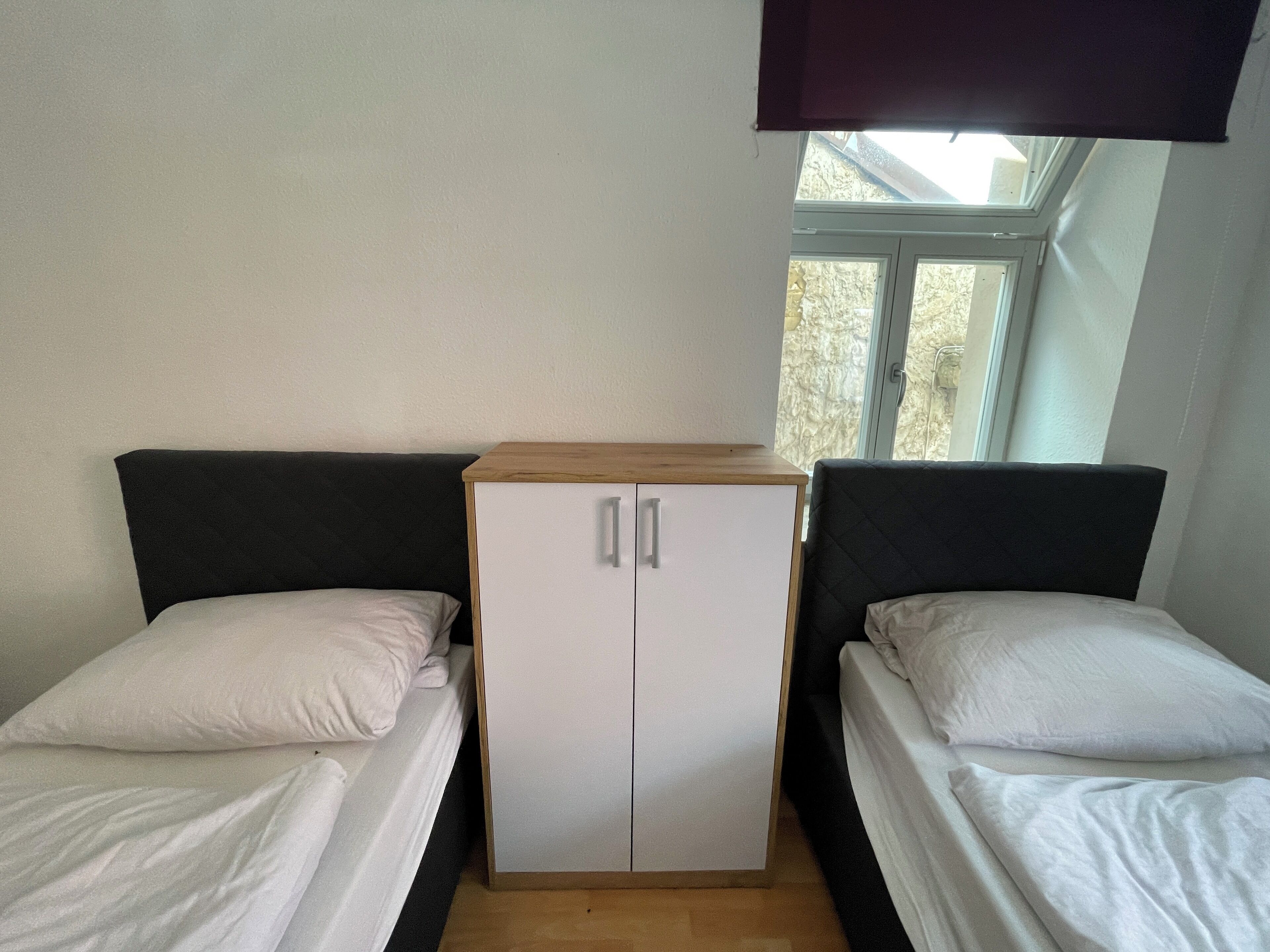 A room with two single beds, a wardrobe, and a window with a view of trees.
