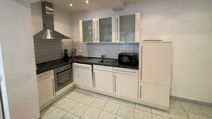 A modern kitchen with white cabinets, a black countertop, a built-in oven, a microwave, and a stainless steel range hood. - MY-Skypalace Sinsheim (Sinsheim)