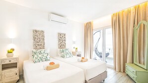 Ein Hotelzimmer mit zwei Betten, einem großen Spiegel, einer grünen Kommode und einem Balkon mit Vorhängen.