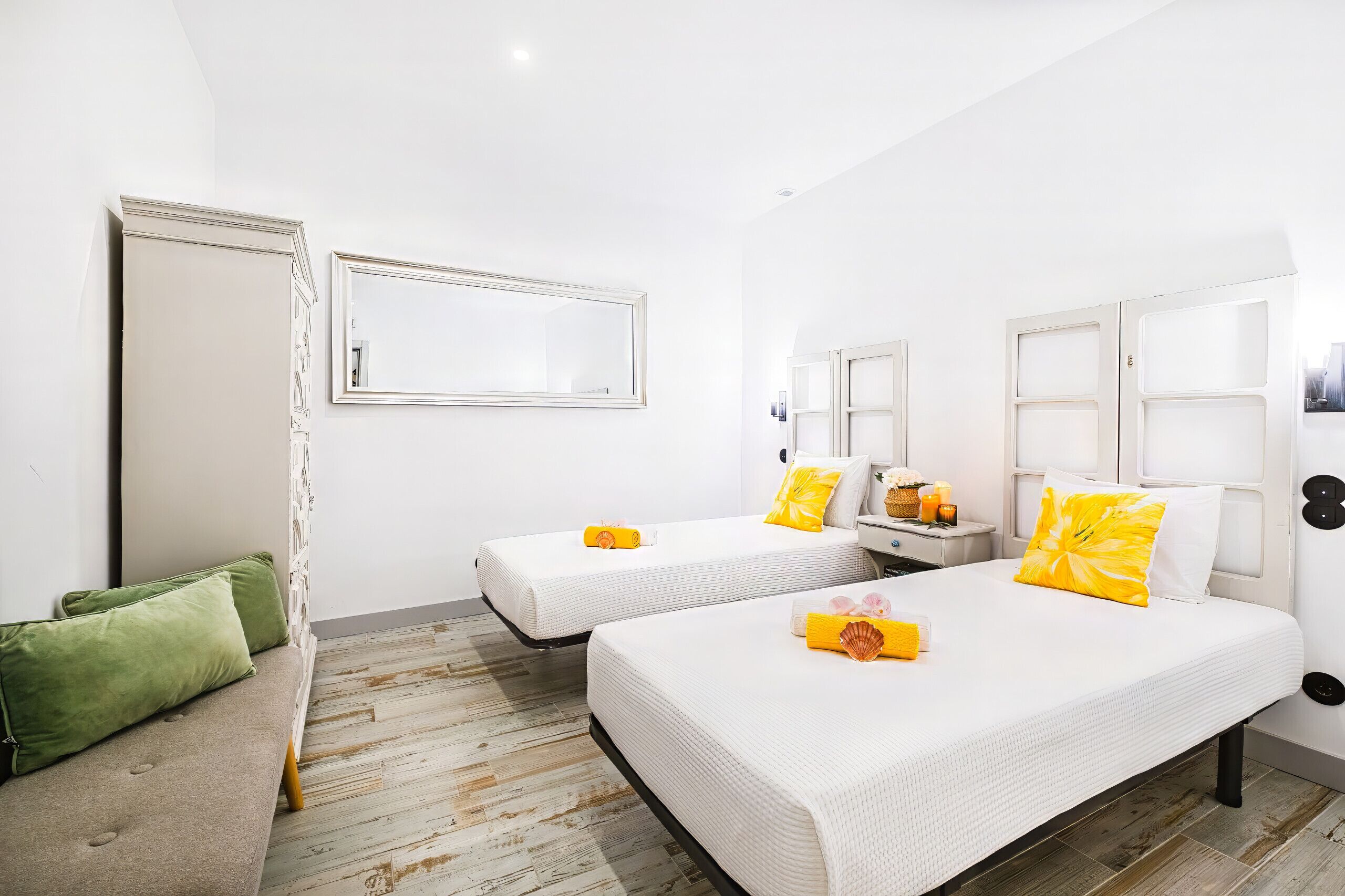 A hotel room with two beds, a sofa, a mirror, and a small table with a basket and orange juice.