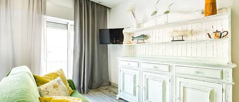 Una sala de estar con un sofá verde, un aparador blanco con objetos decorativos y un televisor de pantalla plana montado en la pared.