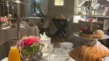 A breakfast setting with a table set for two, featuring a variety of pastries, a pitcher of orange juice, and a floral arrangement.