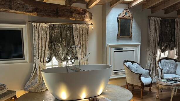 Une salle de bain moderne avec une grande baignoire éclairée, un plafond en bois et un fauteuil classique.